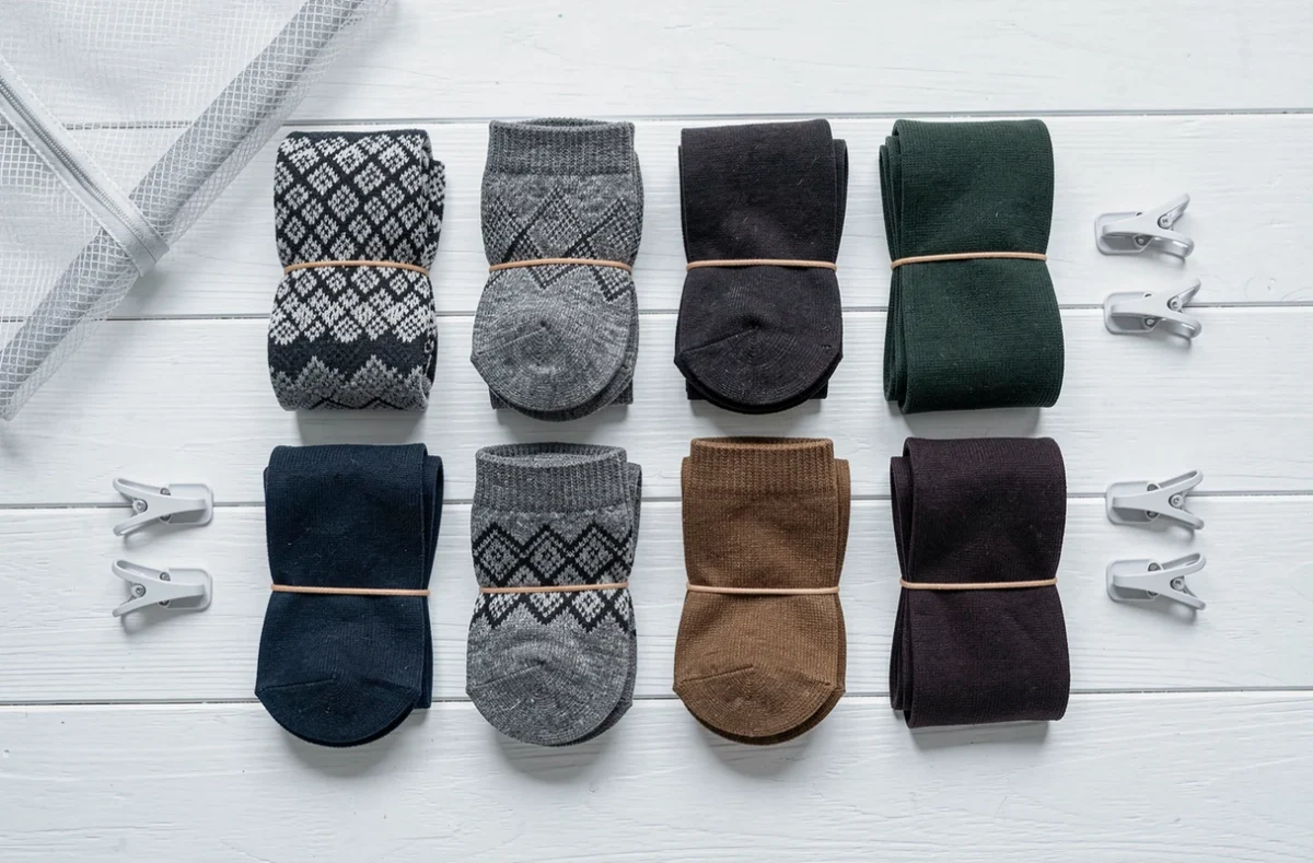 Vue de dessus d'une collection de paires de chaussettes assorties et organisées sur une surface en bois blanc avec accessoires de rangement